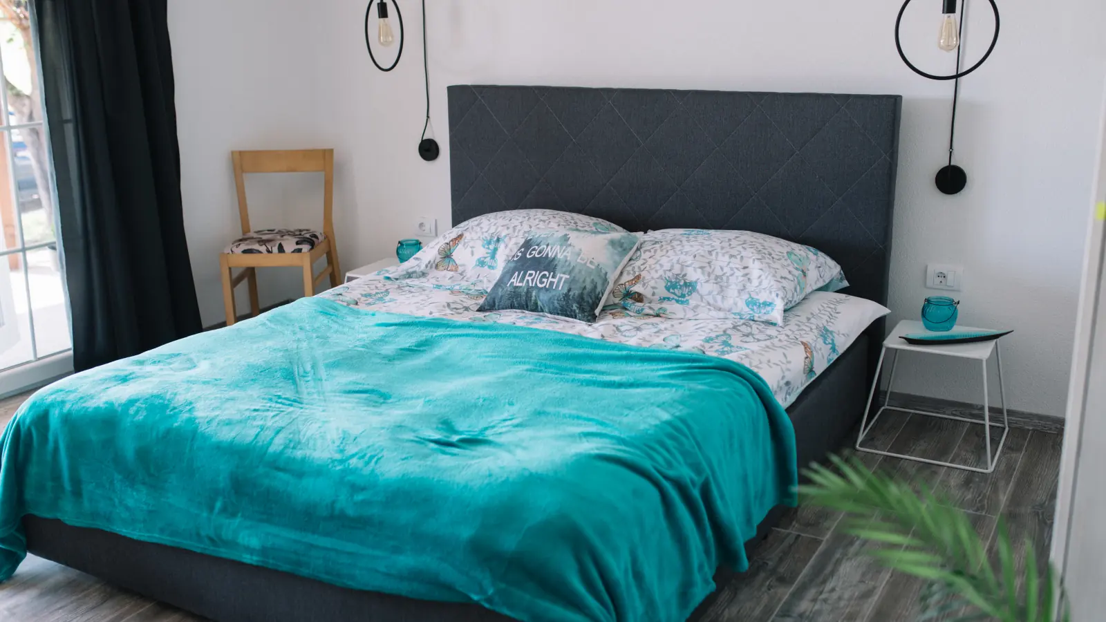 A bright, tidy double bedroom with a teal throw on the bed